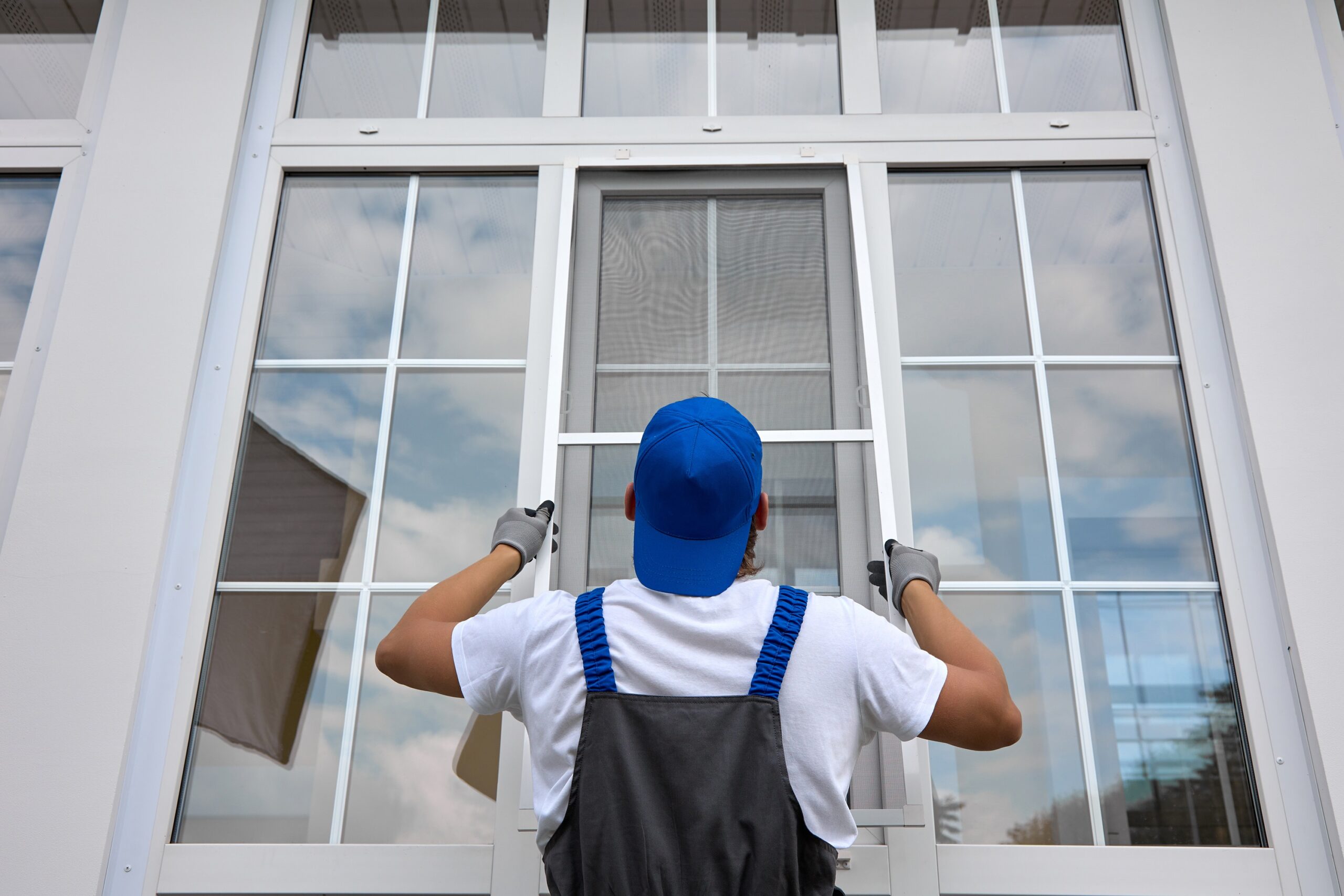 Experienced worker holds mosquito net in his hands, professionally installs it on window outside building. Professional installation of protective nets against insects on plastic windows of any size